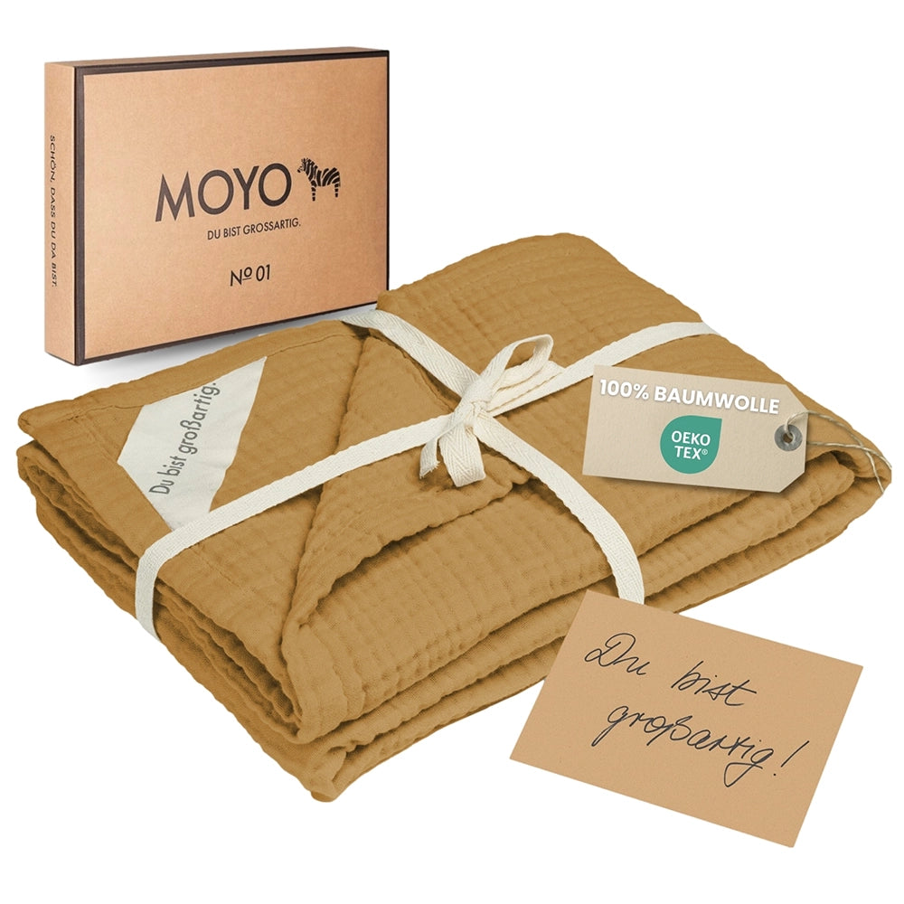 MOYO Musselin Decke in Ocker in der nachhaltigen Geschenkverpackung – bereit zum Verschenken.