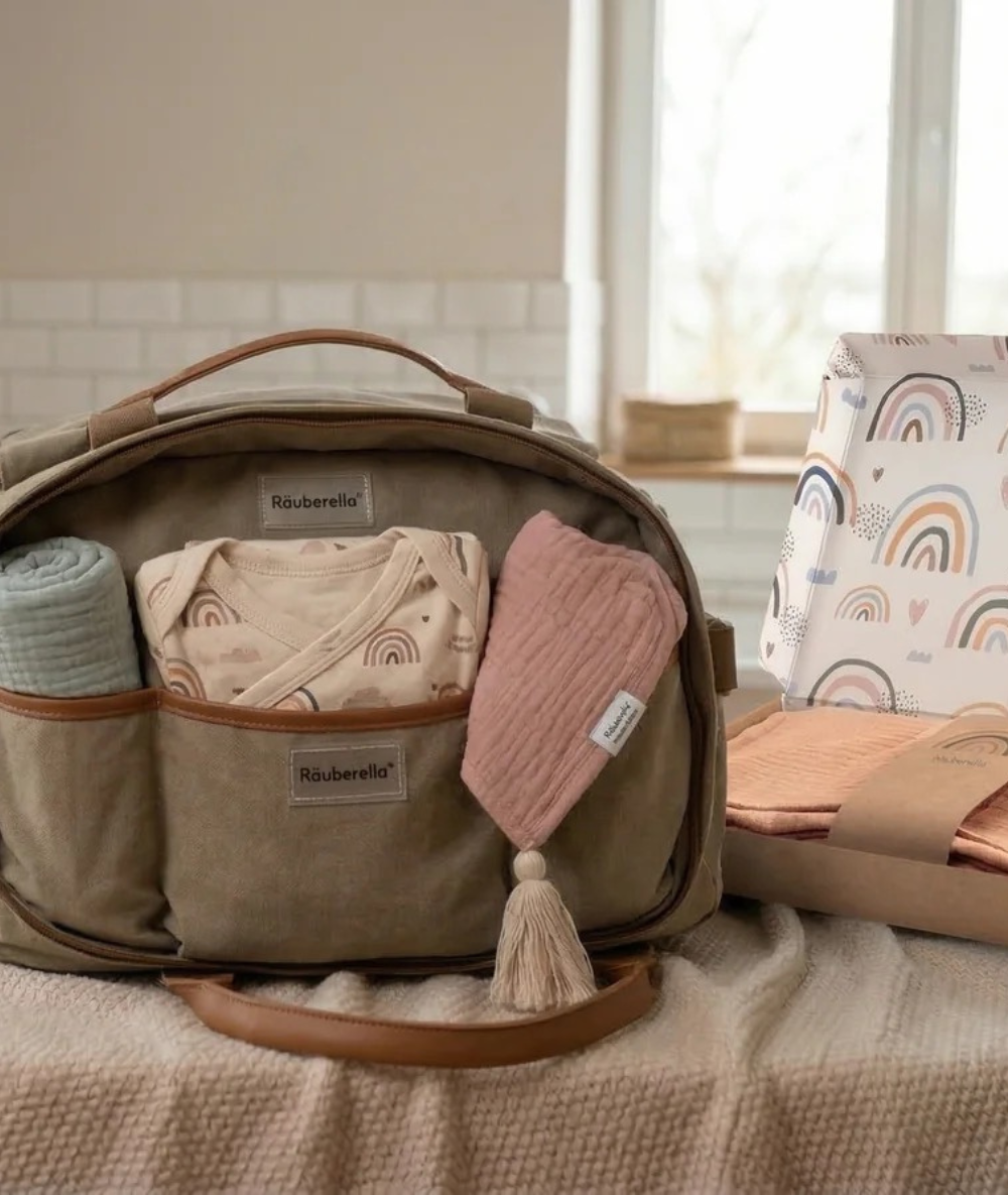 Gepackte Räuberella Wickeltasche in Salbeigrün mit Baby-Erstausstattung wie Body, Mulltüchern und Regenbogen-Box für den Frühlingsausflug.