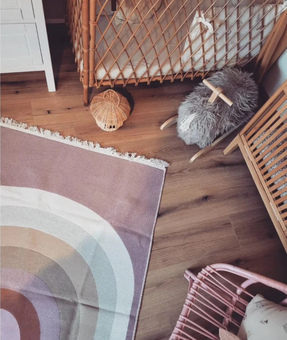Einladendes Kinderzimmer-Interieur mit Holzparkett, einem Regenbogen-Teppich in sanften Pastellfarben und einem flauschigen Schaukel-Schaf zur Beruhigung und Entspannung des Babys.